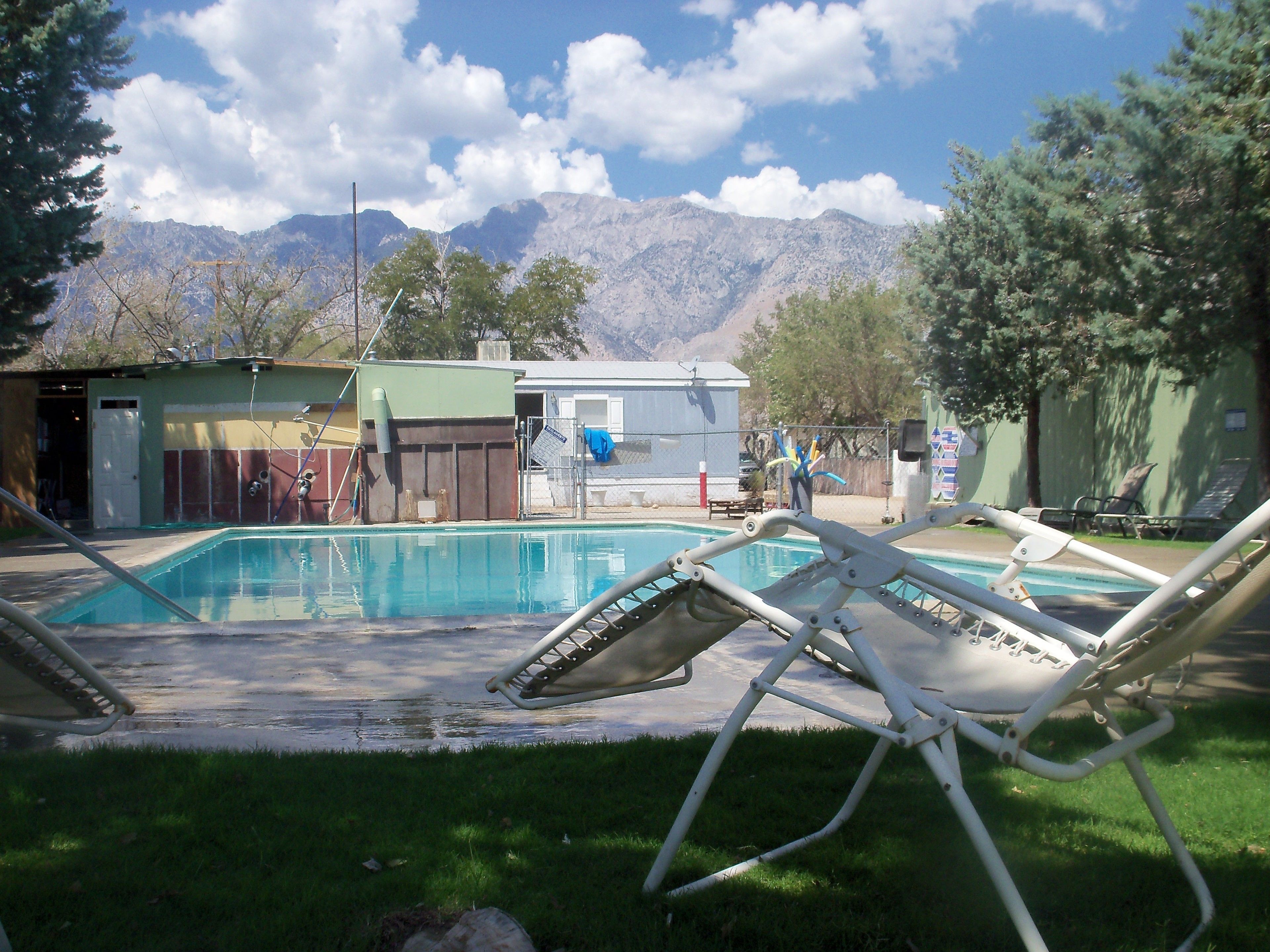 A swimming pool with lounge chairs, a small building, and mountains in the background.