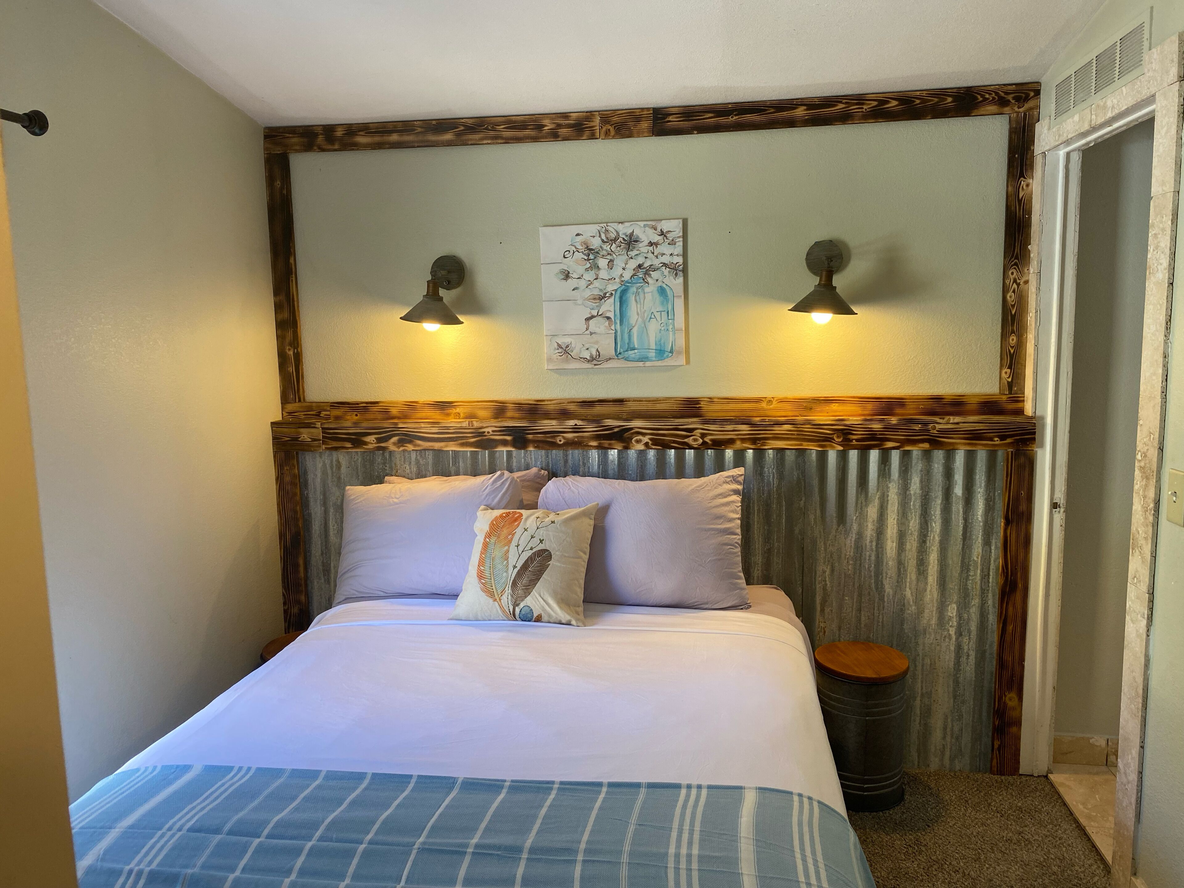 Een bed met hoofdeinde, twee wandlampen en een schilderij erboven.