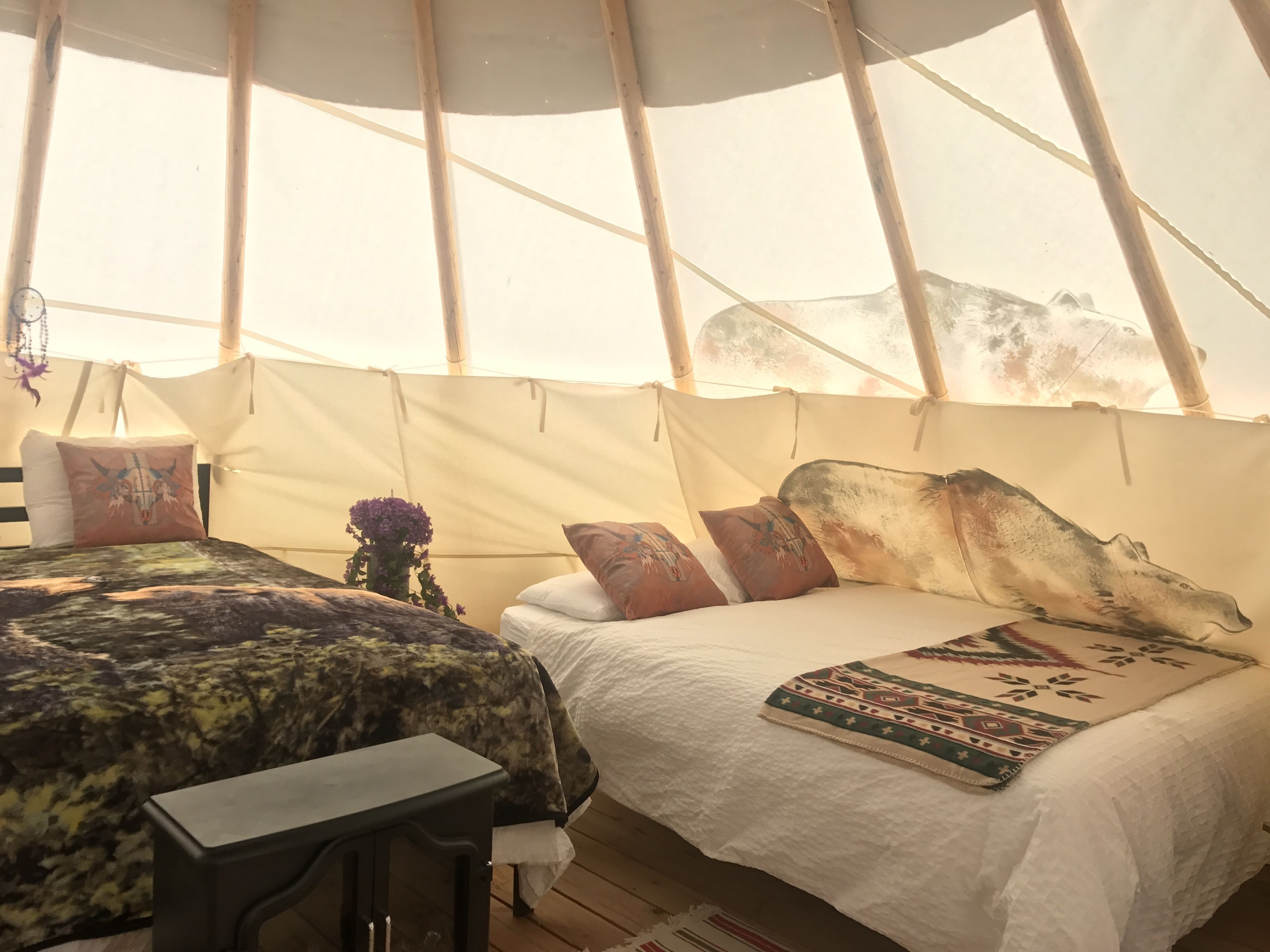 A tent with two beds, each with patterned bedding and pillows, and a small table.