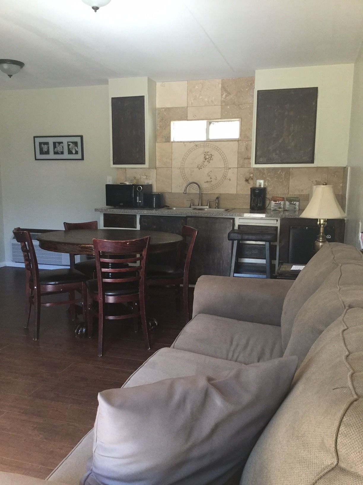 A living room with a sofa, a dining table with chairs, a kitchen area with a microwave, toaster, and coffee maker, and a window with a view of the outdoors.