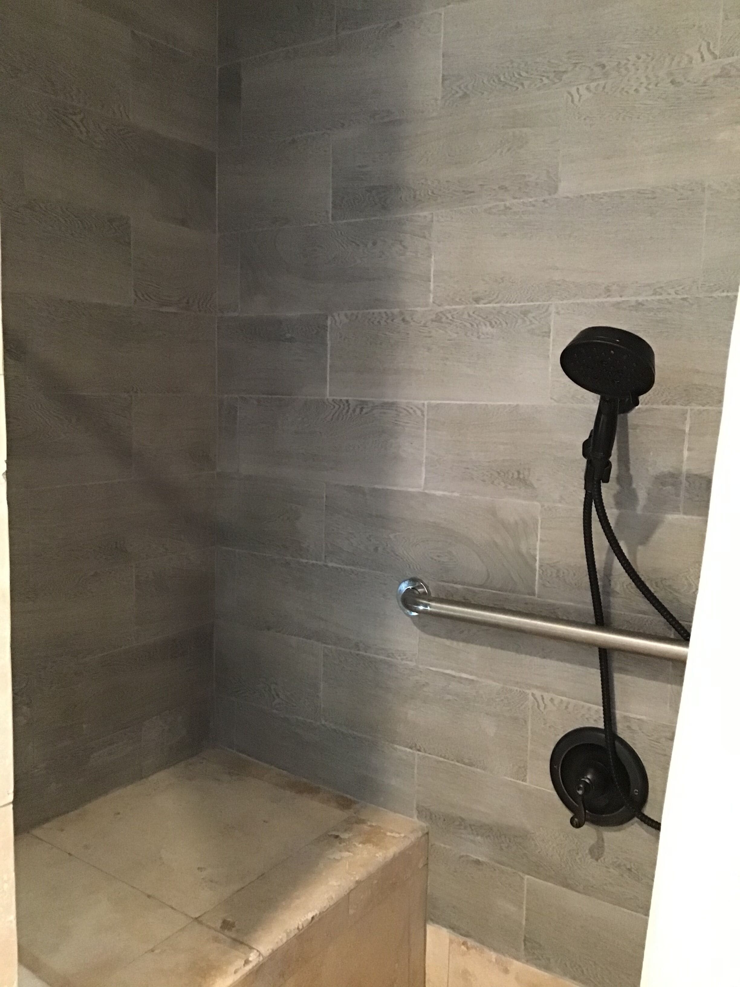 A shower area with a tiled wall, a metal handrail, and a black faucet.