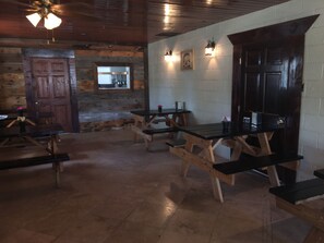 A rustic interior with wooden tables and benches, a stone wall, and a wooden door.