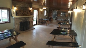 Un coin repas rustique avec des tables et des bancs en bois, une cheminée en pierre et des luminaires fixés au mur.