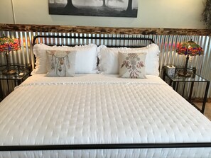 A neatly made bed with a quilted white bedspread and decorative pillows, flanked by two nightstands with lamps.