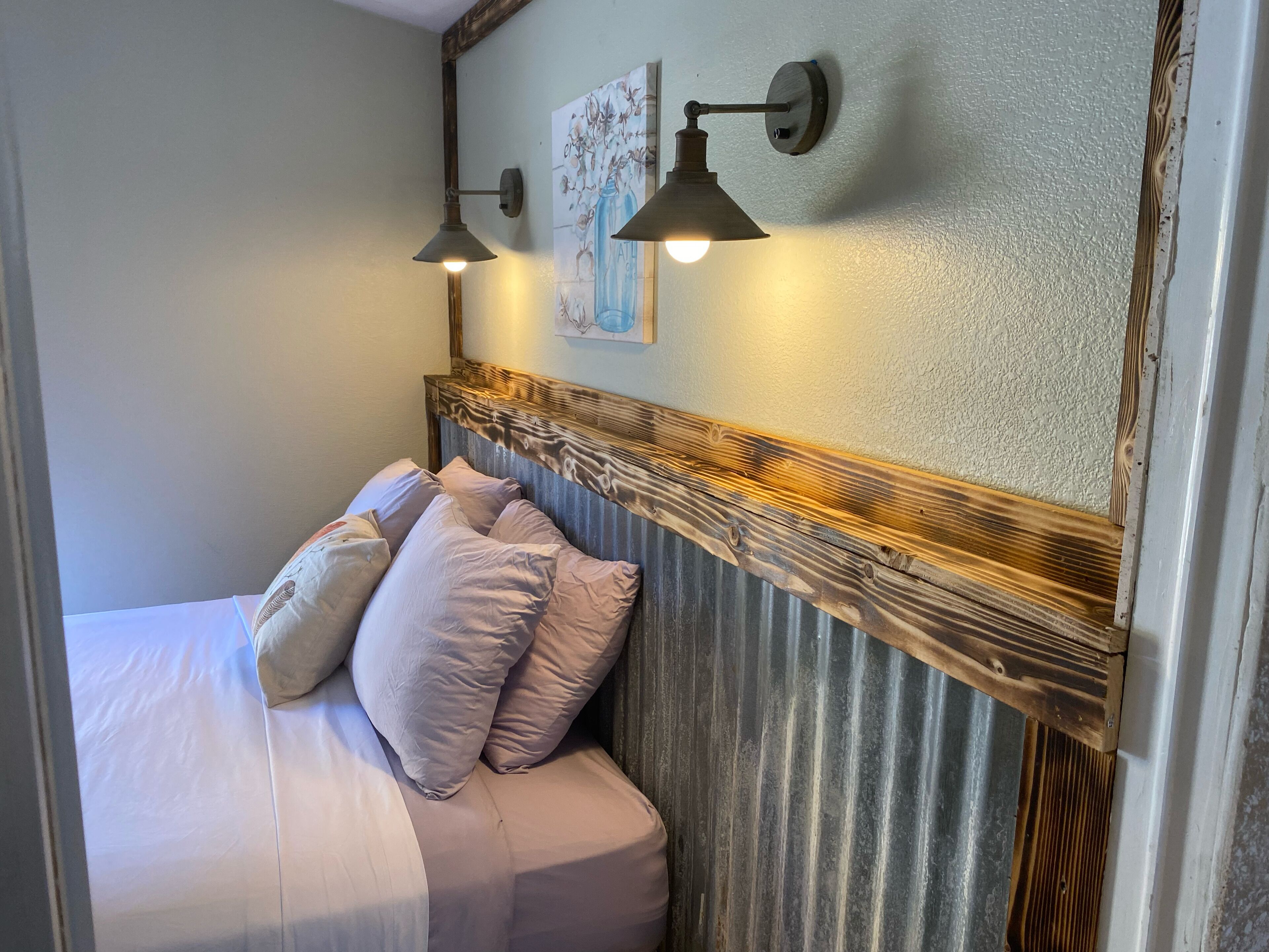 A bedroom with a bed, pillows, a headboard, and two wall-mounted lamps.