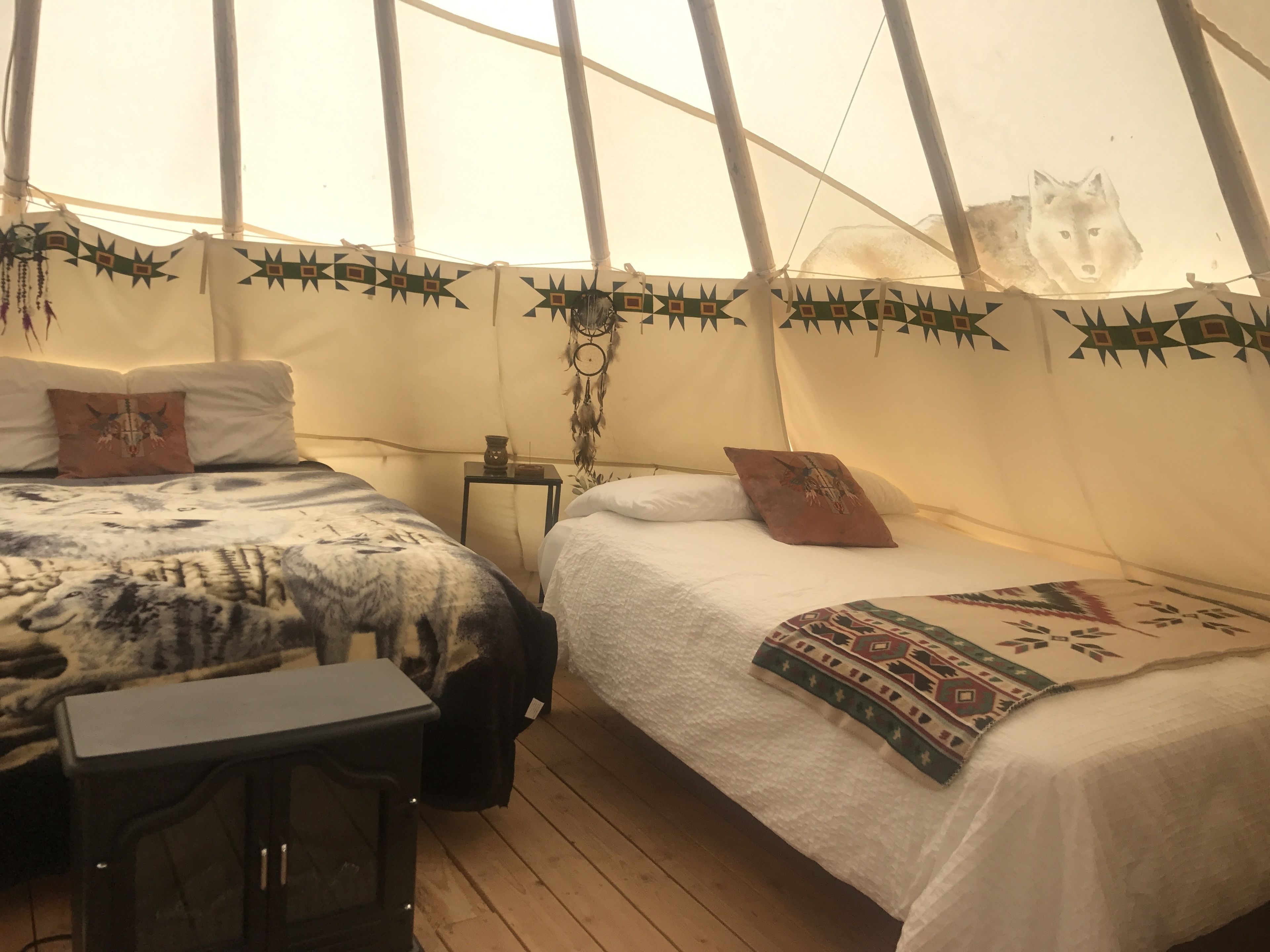 A tented accommodation with two beds, a small table, and a heater.