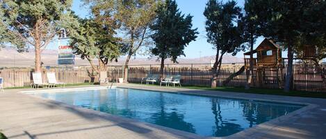 Una piscina rectangular con plataforma de madera, rodeada de árboles y una cerca de madera.