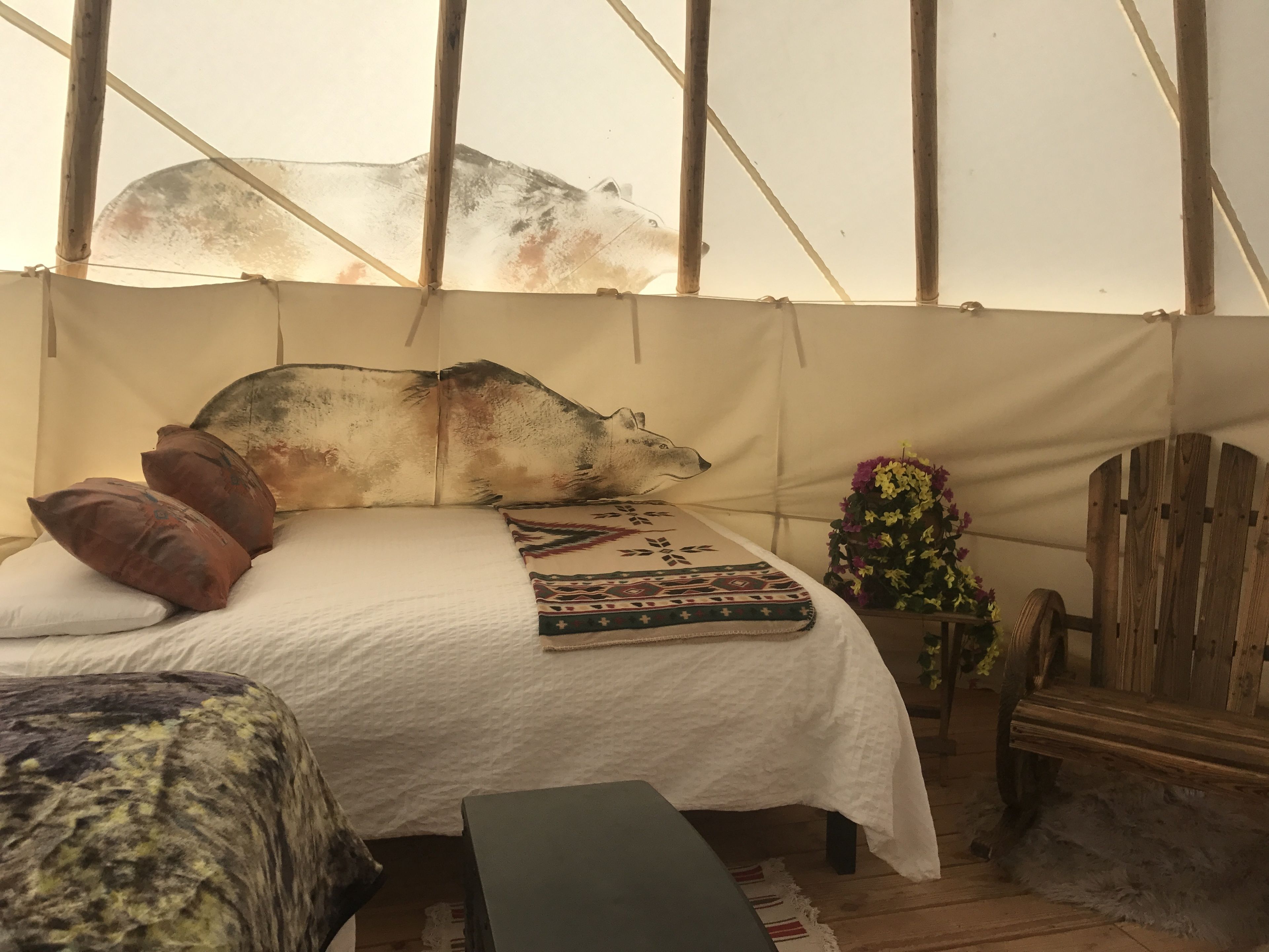 A tented room with a bed, pillows, a blanket, a chair, and a wooden bench.