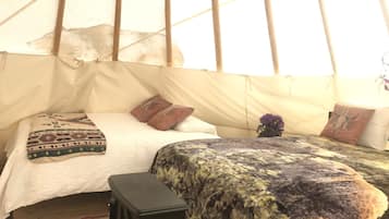 A cozy interior with a bed, pillows, a small cabinet, and a window.
