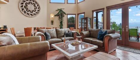 A spacious living room with leather sofas, a coffee table, and a large window offering a view of the outdoors.