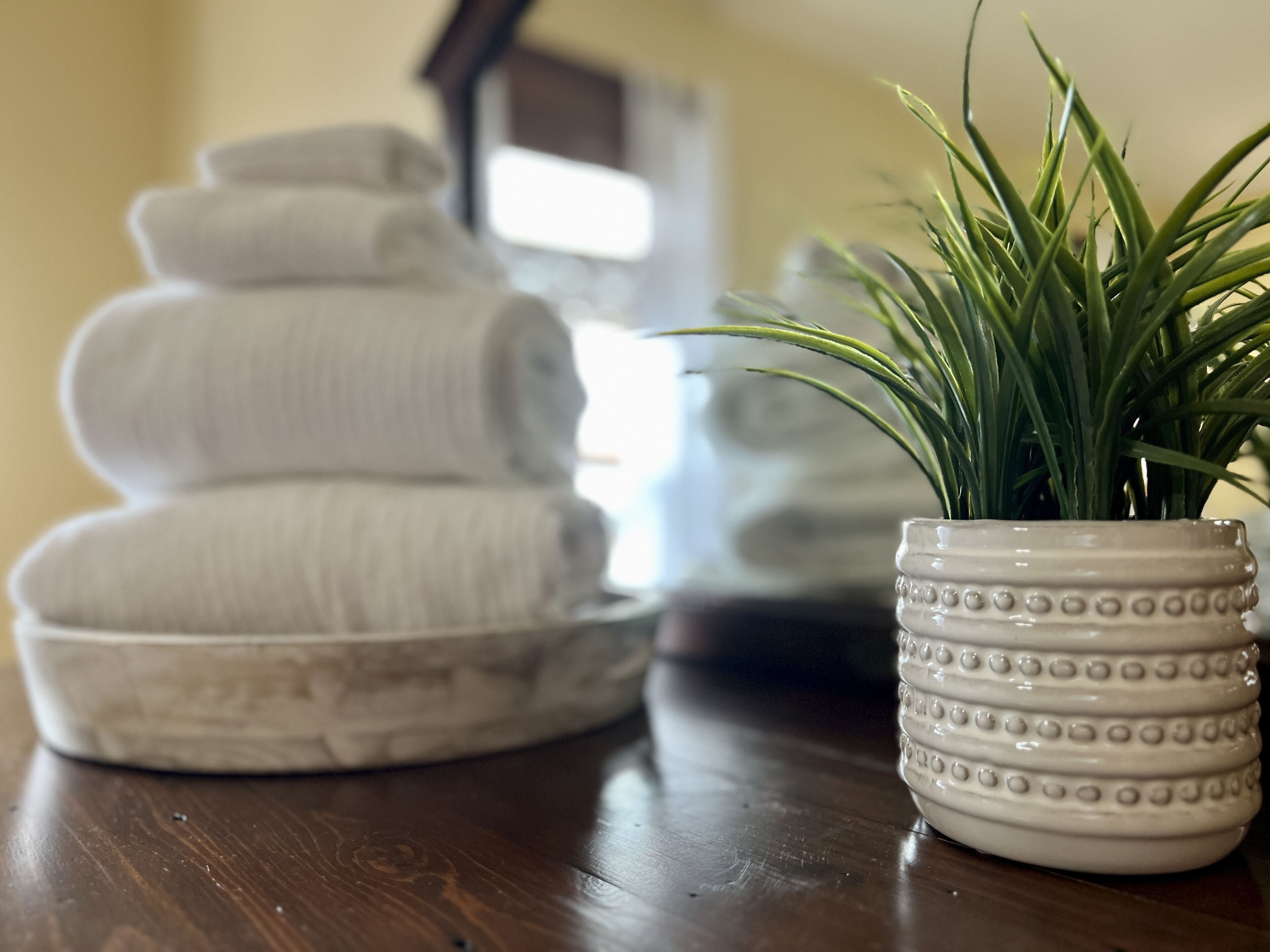 A stack of folded towels and a potted plant on a wooden surface.