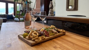 A wooden table with a charcuterie board, wine glasses, and a bottle of wine in a room with a view, a clock, and a mirror on the wall. - Casa Grande Inn (Penticton)