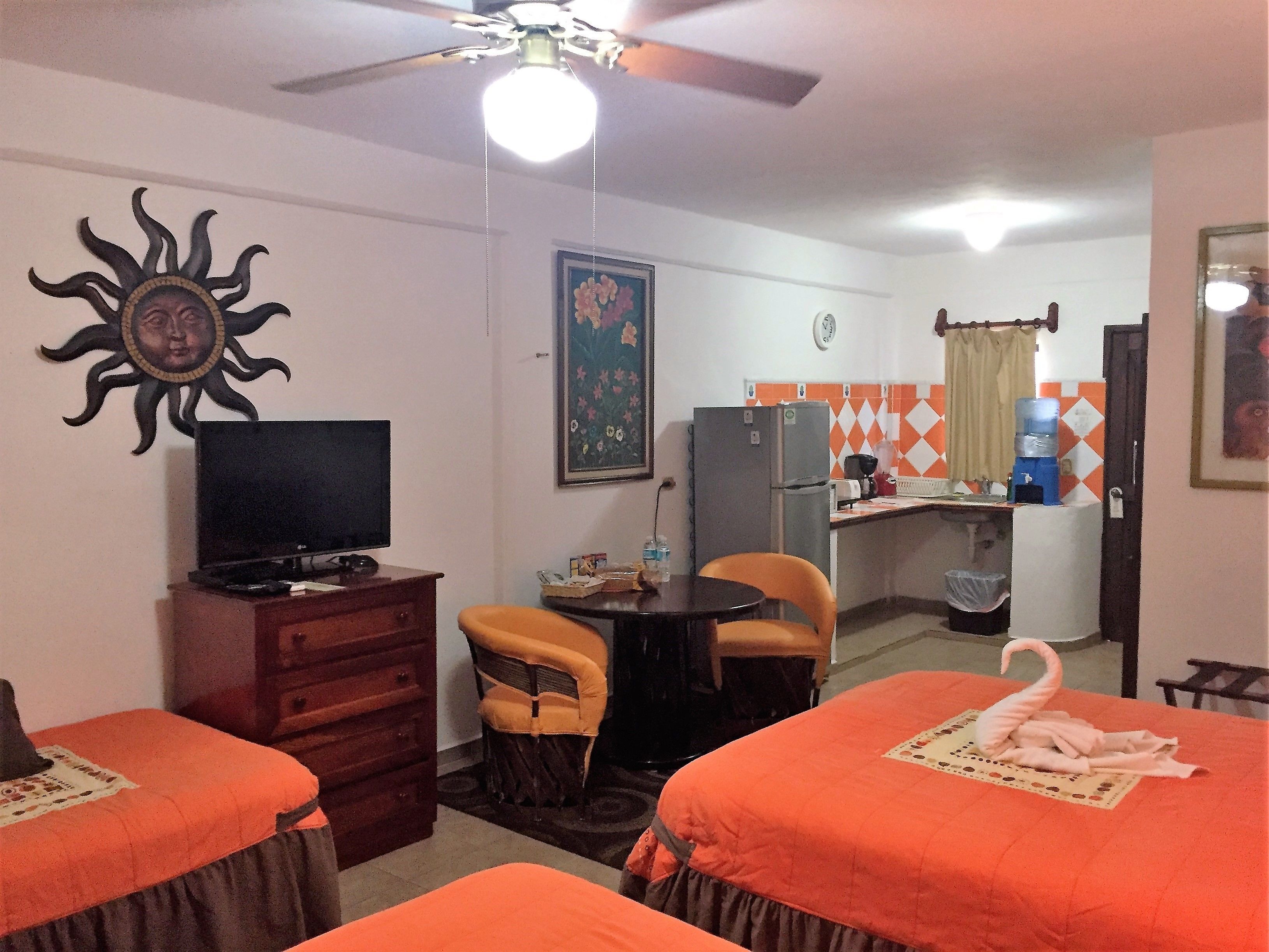 A hotel room with two beds, a television, a desk with a refrigerator, and a small kitchen area.