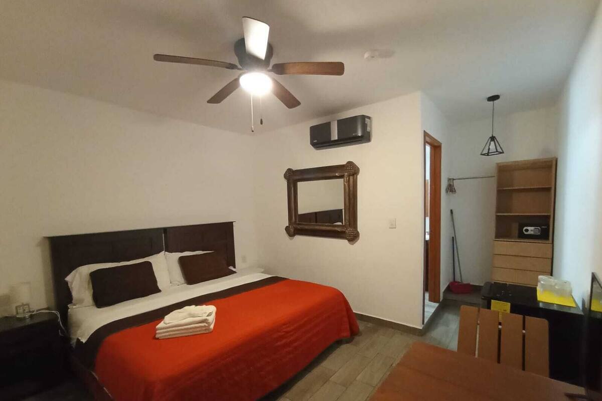 Una habitación de hotel con una cama, un ventilador de techo, un espejo y un armario de madera.