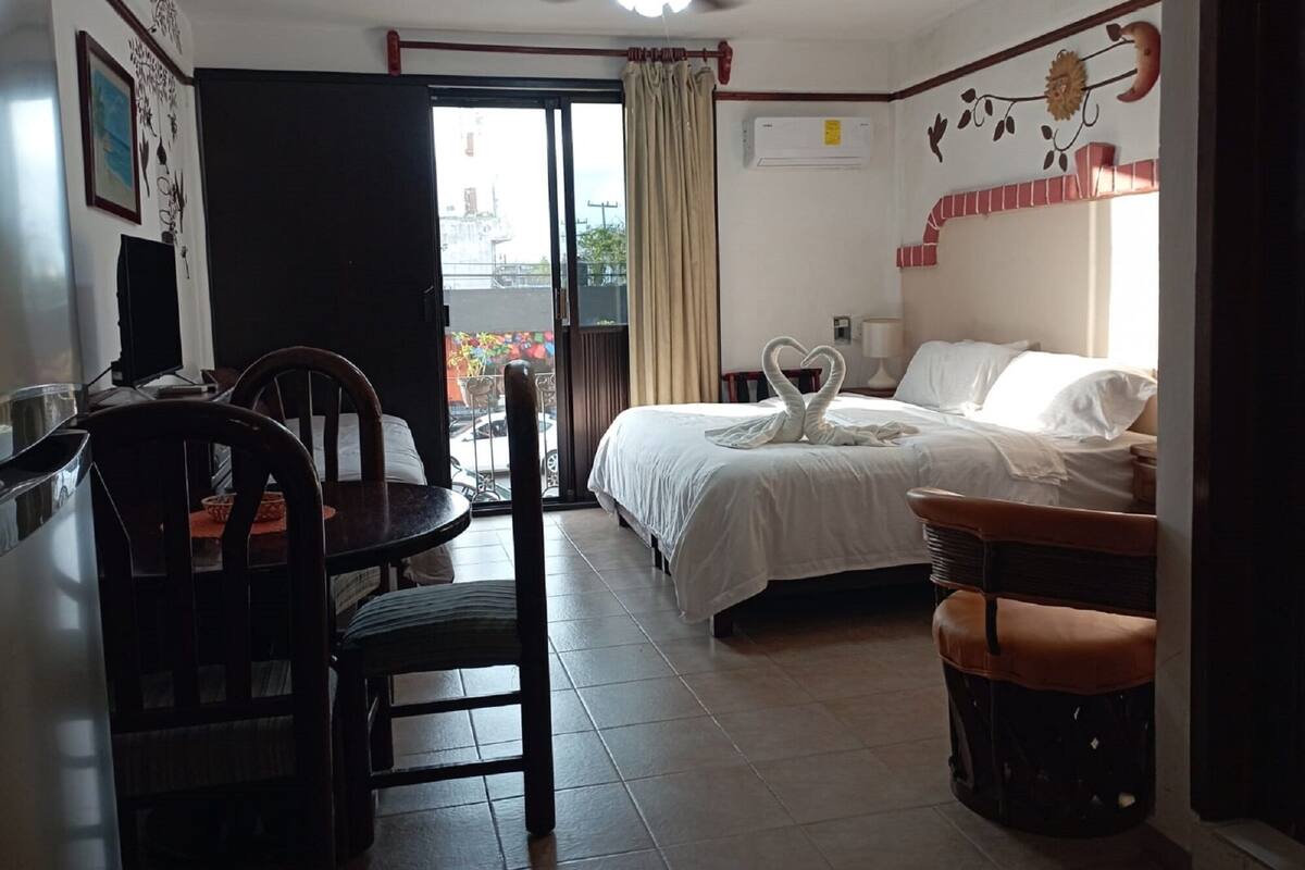 Habitación de hotel con cama, escritorio, silla, ventilador de techo y vistas al exterior.