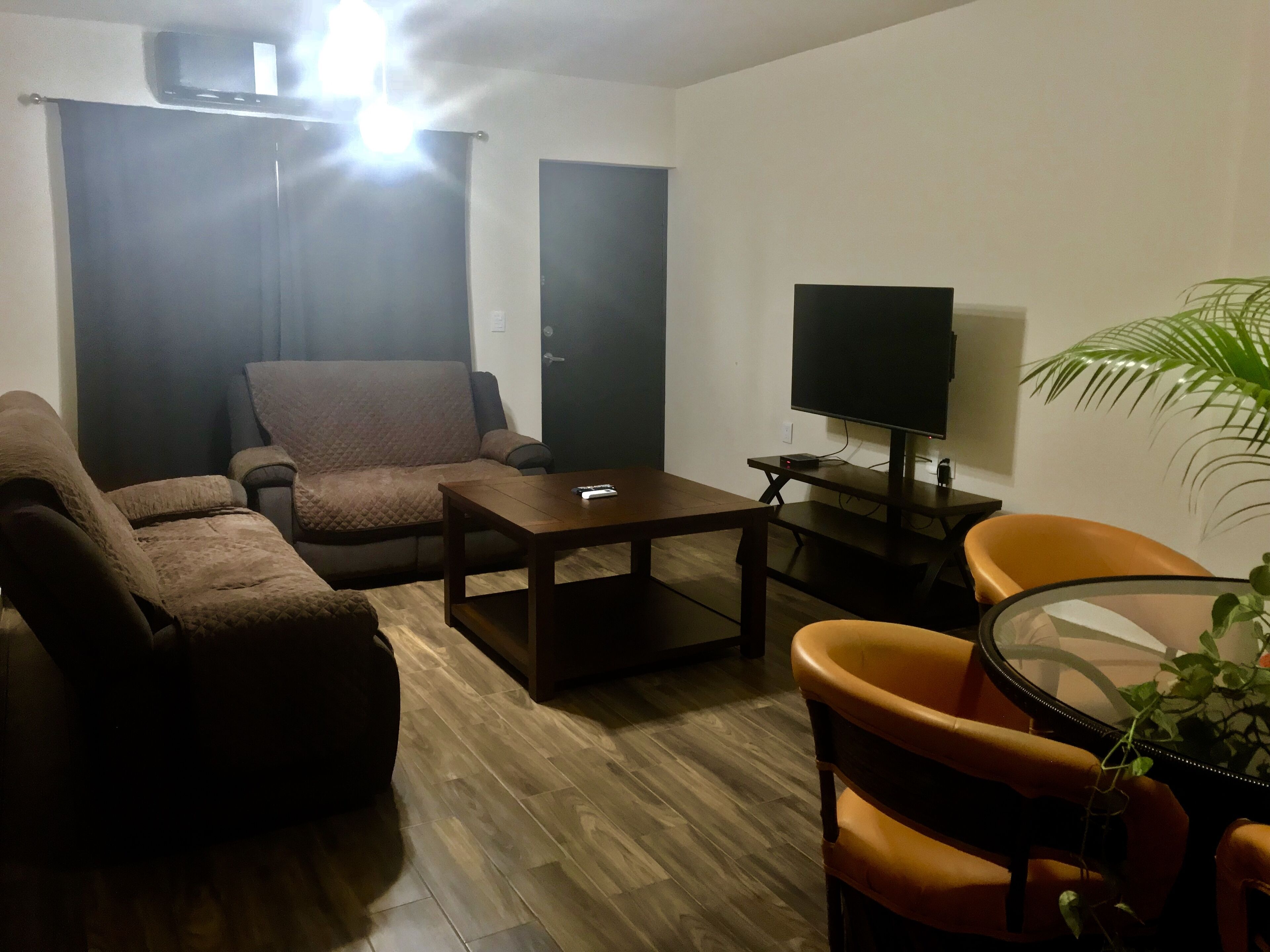 Un salon comprenant un canapé, des fauteuils, une table basse, un téléviseur et une plante.