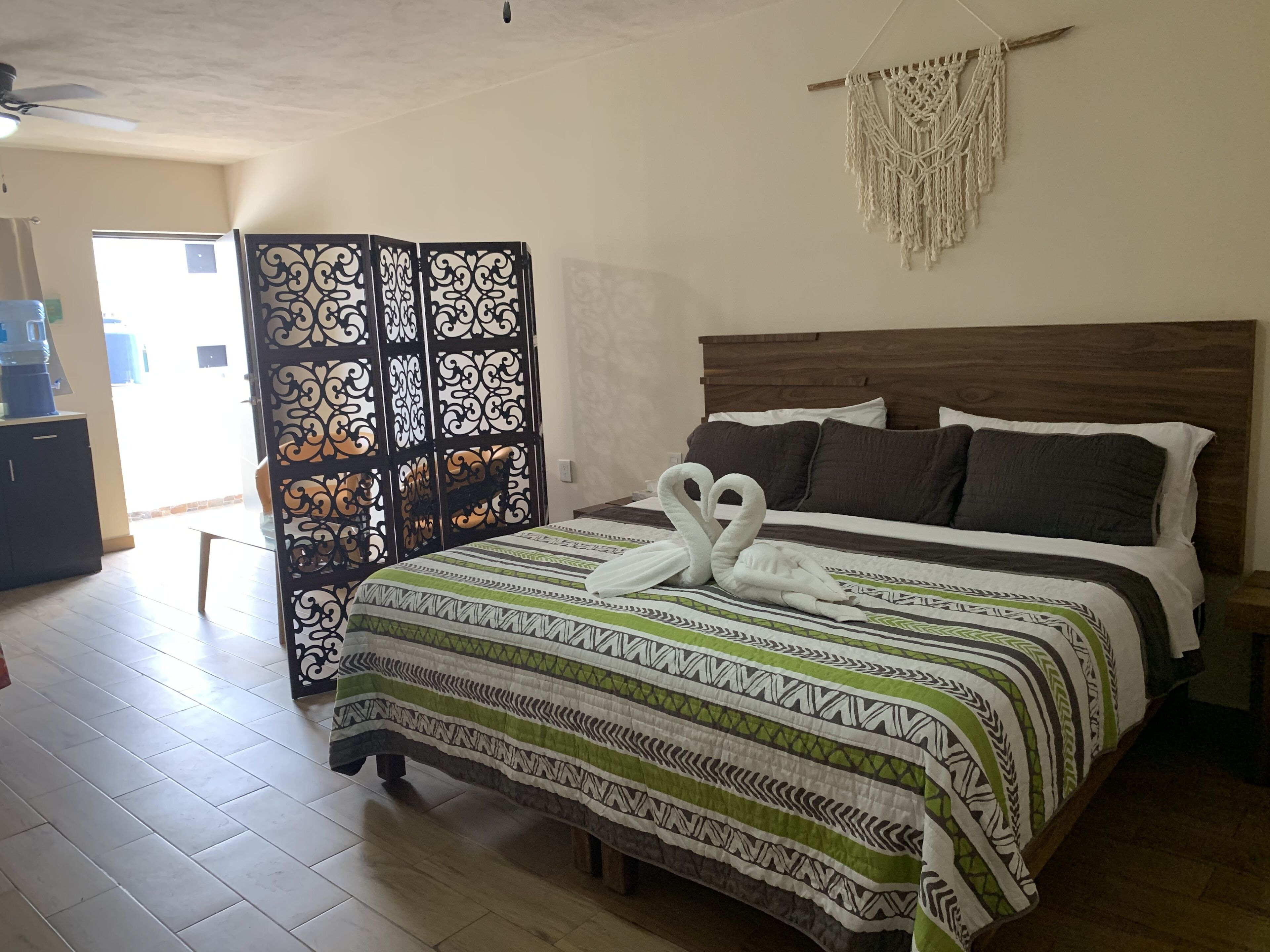 A hotel room with a bed, a decorative macrame wall hanging, and a view of the outside.