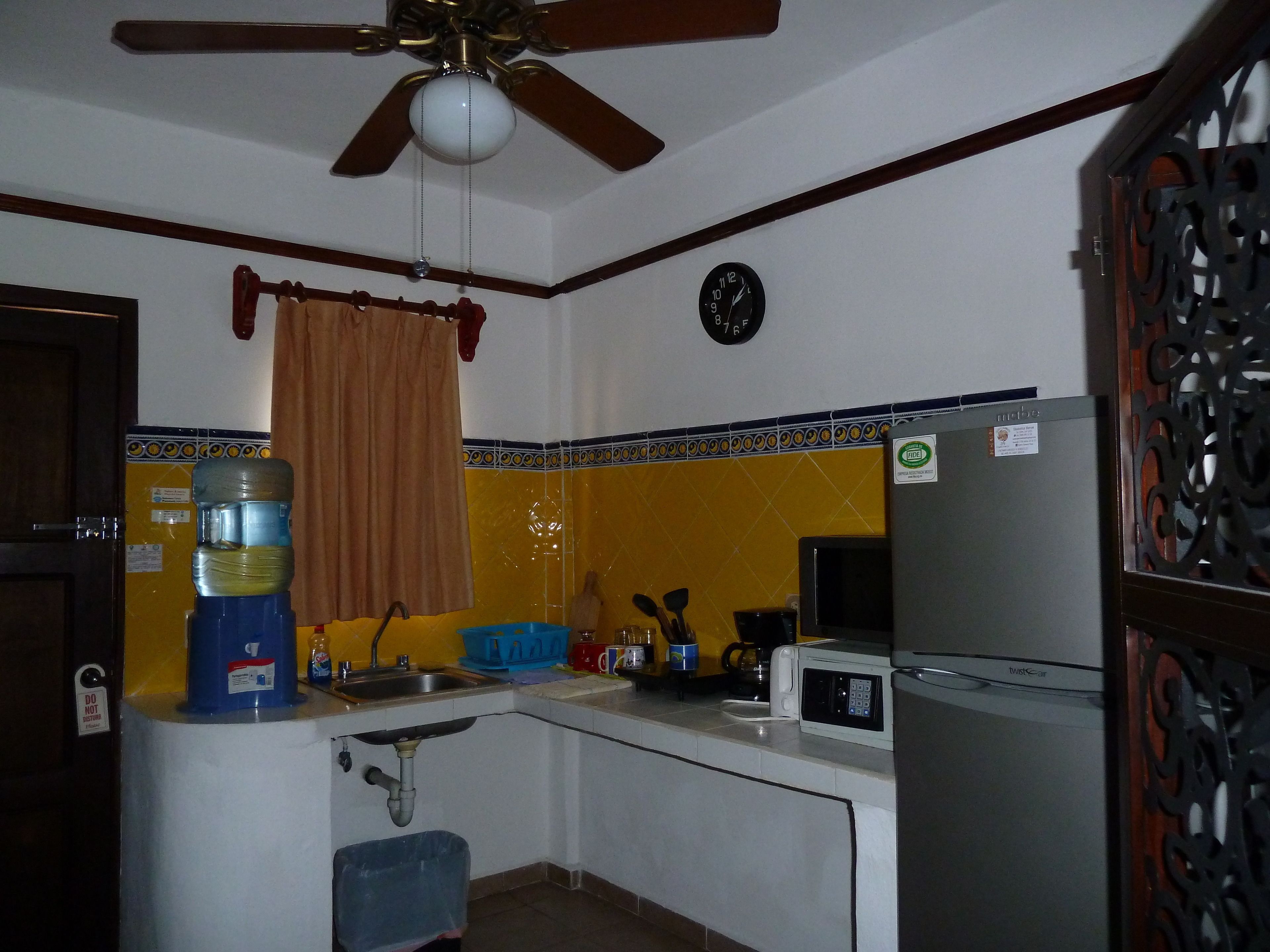 A compact kitchen with a ceiling fan, a sink, a microwave, and a refrigerator.