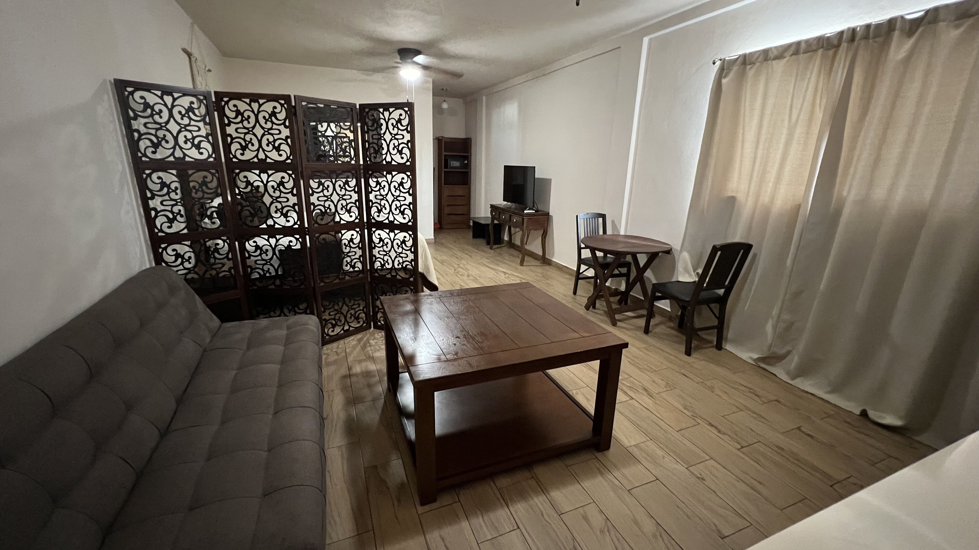 A living room with a sofa, a coffee table, a TV, and a dining area with chairs.