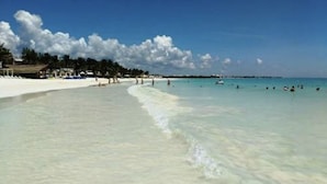 A beach with clear turquoise water, white sand, and a few people swimming. - Suites Fenicia (Playa del Carmen)
