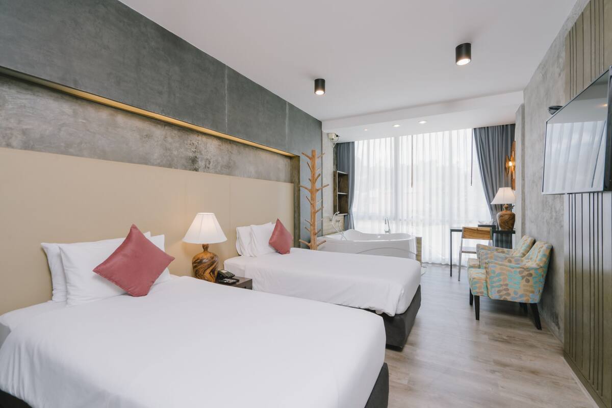 Ein Hotelzimmer mit zwei Betten, einem Schreibtisch, einem Stuhl und einem großen Fenster mit Vorhängen.