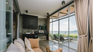A modern living room with a sofa, a glass coffee table, and a view of the sea through large windows. - Patong Signature Boutique Hotel (Patong)