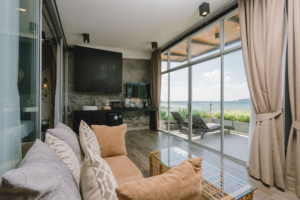 A modern living room with a sofa, a glass coffee table, and a view of the sea through large windows.