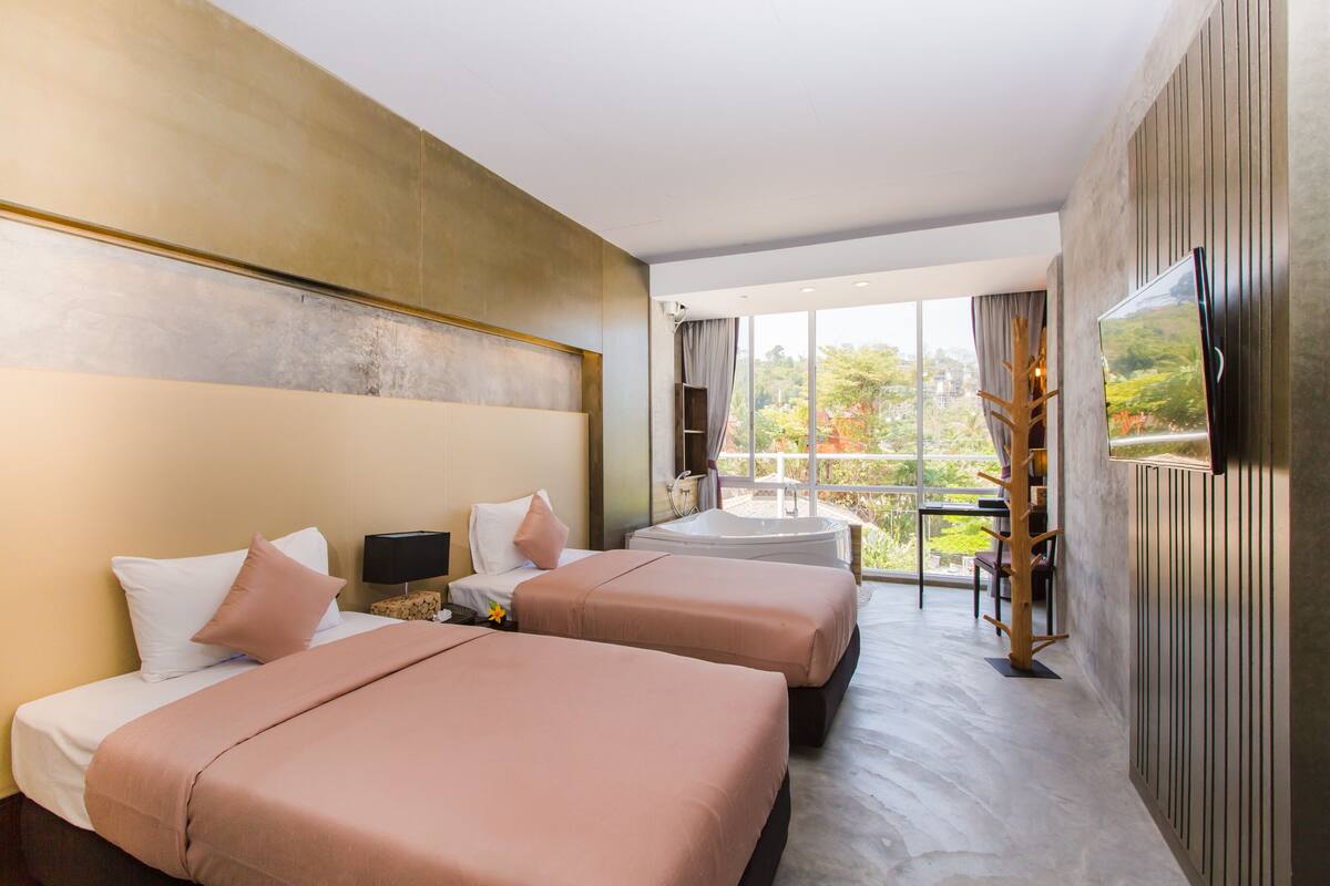 Ein Hotelzimmer mit zwei Betten, einem großen Fenster, einer Badewanne und einem Fernseher.