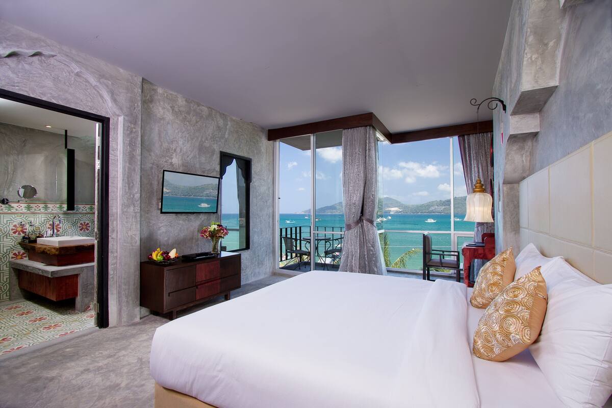 Ein Hotelzimmer mit einem großen Bett, einem Badezimmer mit Waschtisch und einem Balkon mit Meerblick.