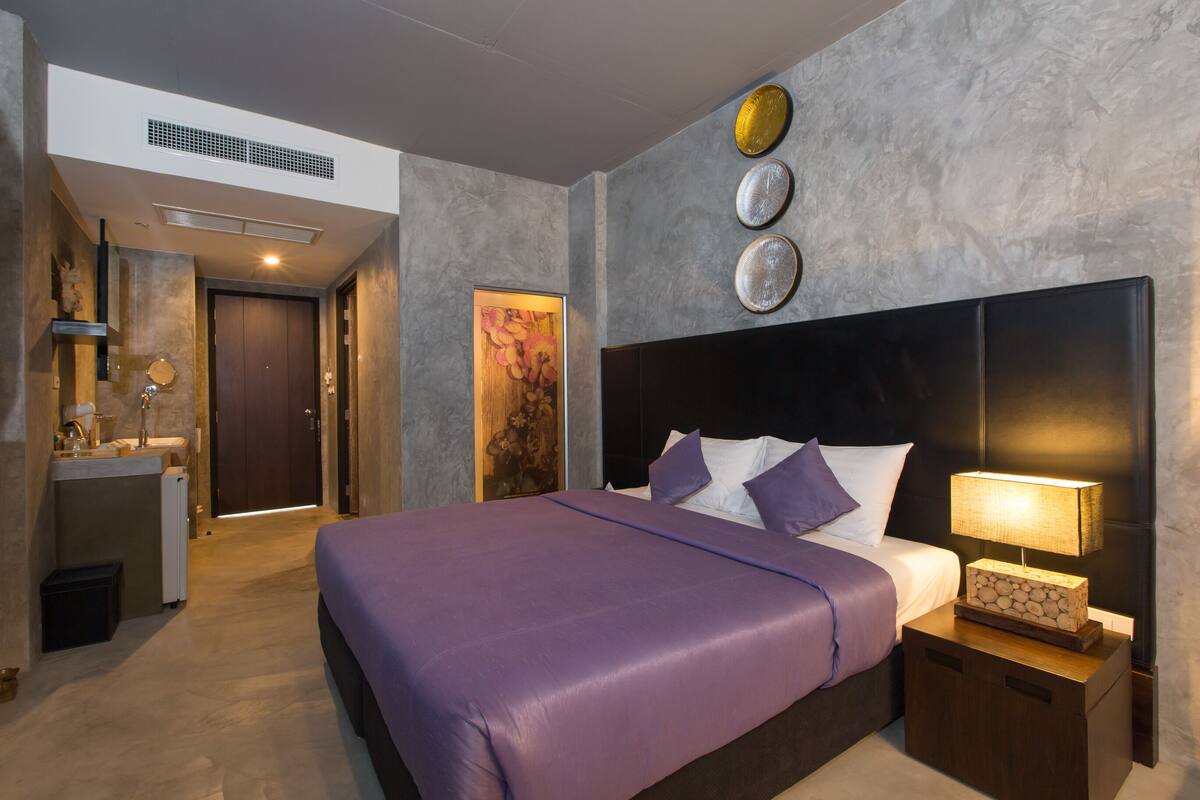Ein modernes Hotelzimmer mit einem großen Bett, einem Nachttisch mit Lampe und einer Wanduhr.