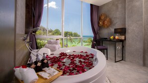 A modern bathroom with a large bathtub filled with rose petals, a vanity with a mirror, and a view of the ocean. - Patong Signature Boutique Hotel (Patong)