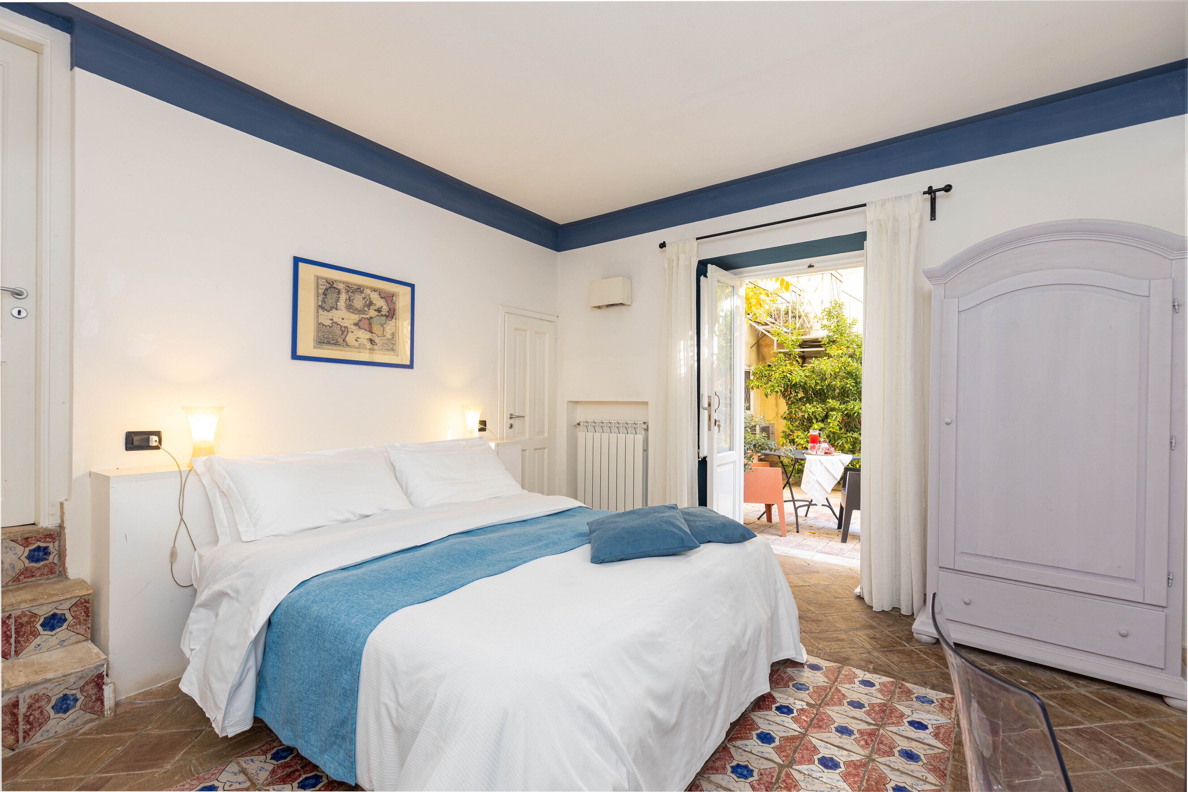 A bedroom with a bed, a painting, a radiator, and a view of the outside.