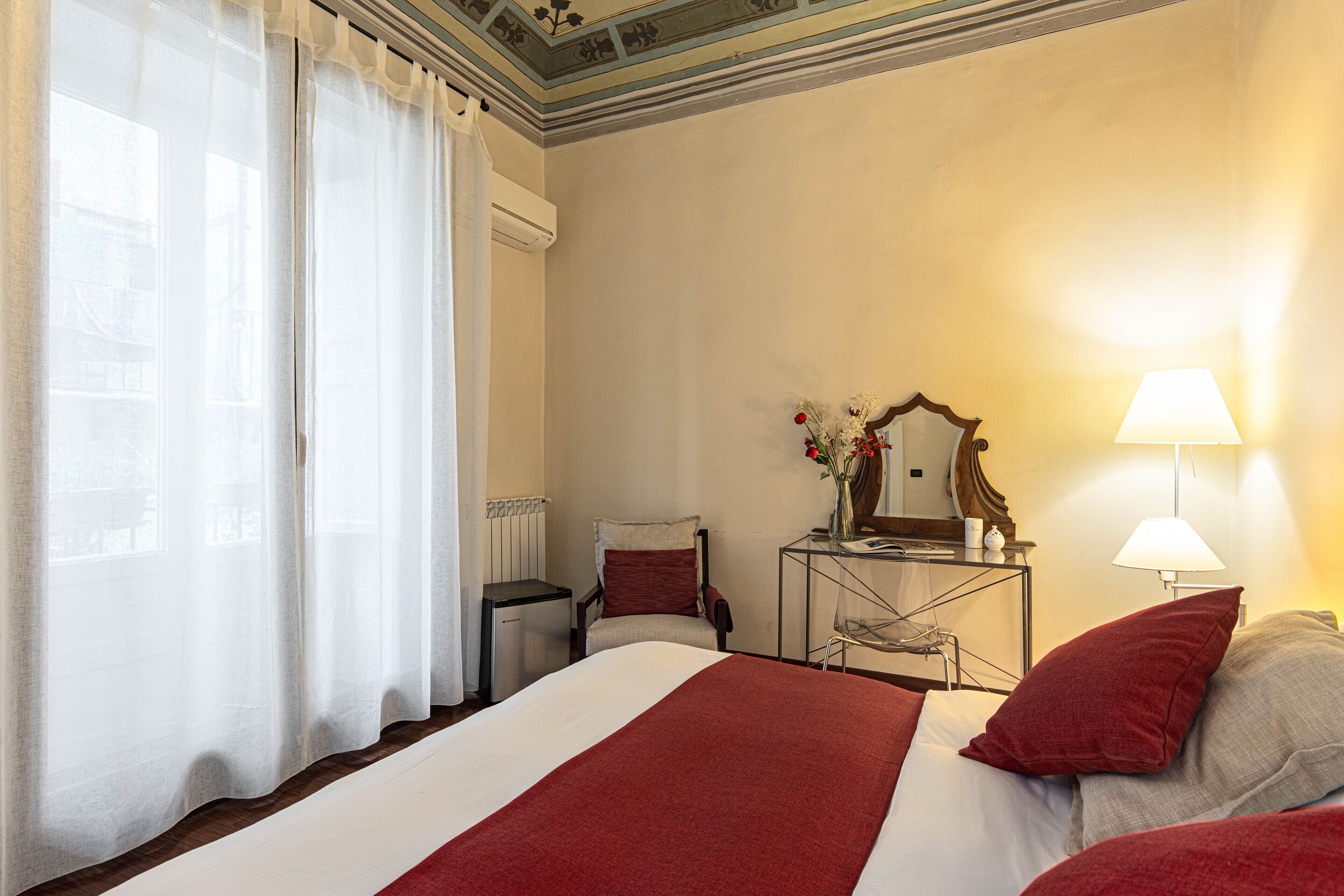 A hotel room with a large bed, a chair, a desk with a lamp, and a mirror.