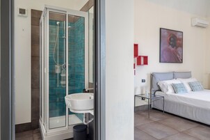 Un bagno moderno con cabina doccia in vetro, un lavandino bianco e un piccolo comodino con lampada.