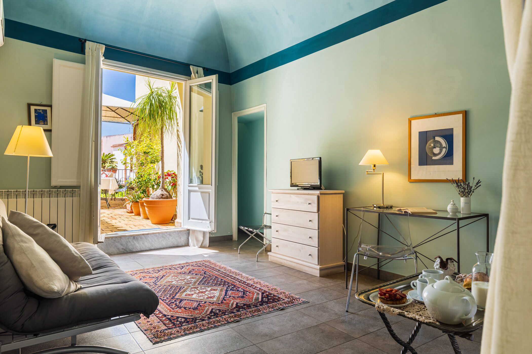 A living room with a sofa, a coffee table with breakfast items, a TV on a stand, and a view of the outside patio.