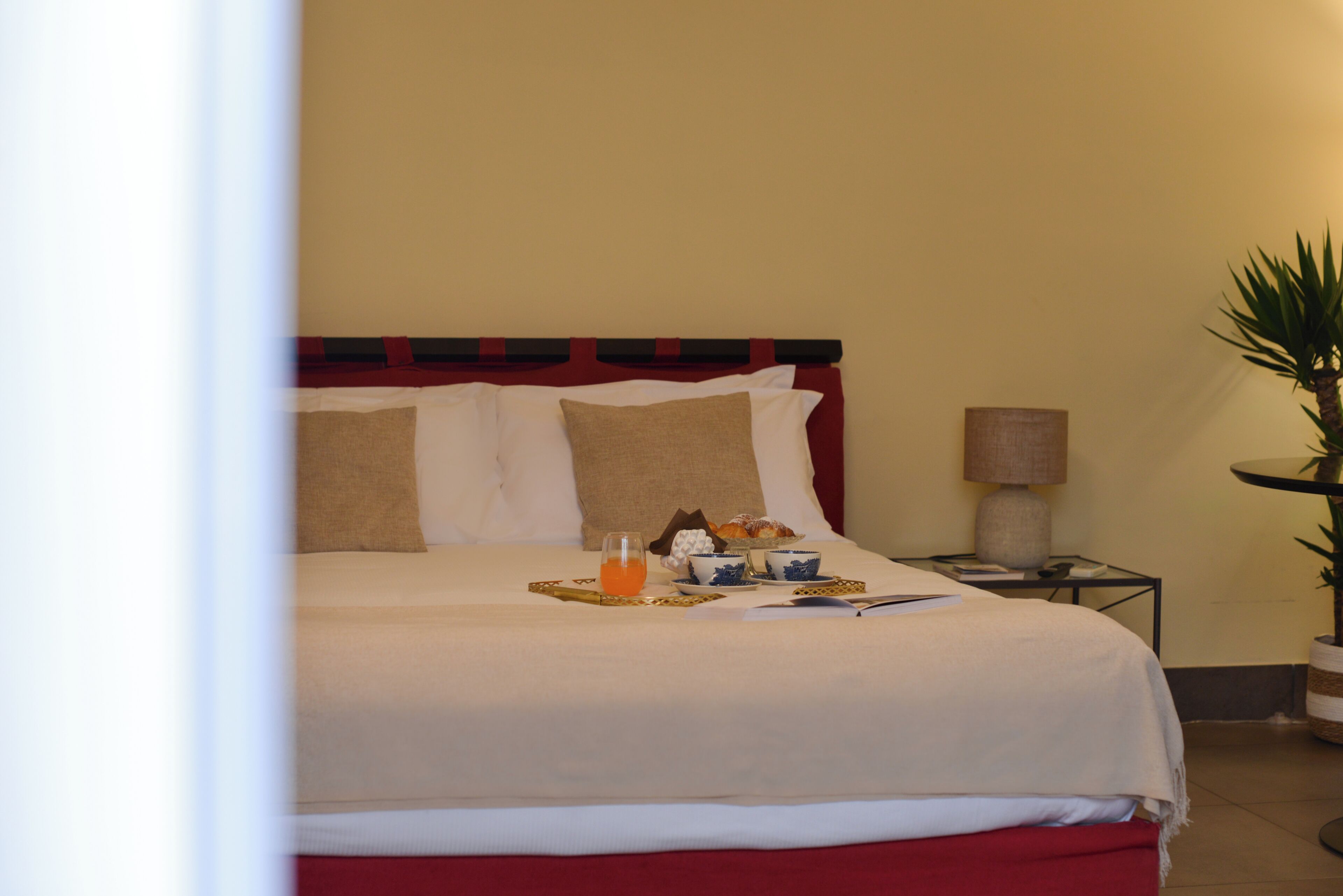 A neatly made bed with pillows, a bedside table with a lamp, and a tray with breakfast items.