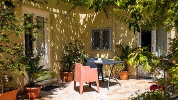 A patio with a table and chairs, surrounded by potted plants and a yellow wall.