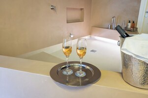 Ein Badezimmer mit einer Badewanne, zwei Champagnergläser auf einem Tablett und einem großen Champagnerflaschen-Behälter.