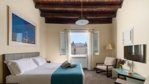 Habitación de hotel con cama, escritorio, silla, ventana con cortinas y un cuadro en la pared, con vistas a edificios.