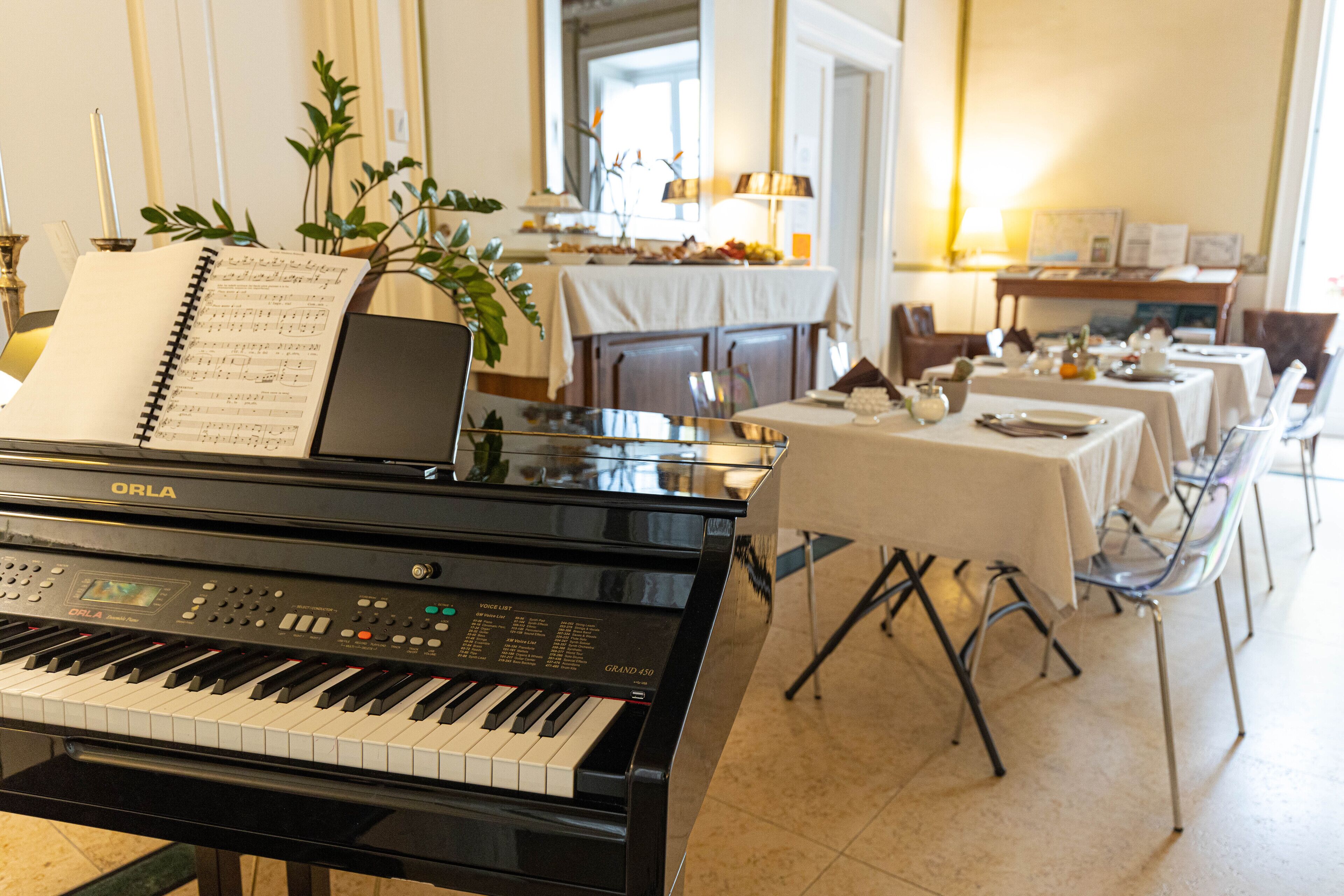A piano with sheet music, a dining area with tables and chairs, and a plant.