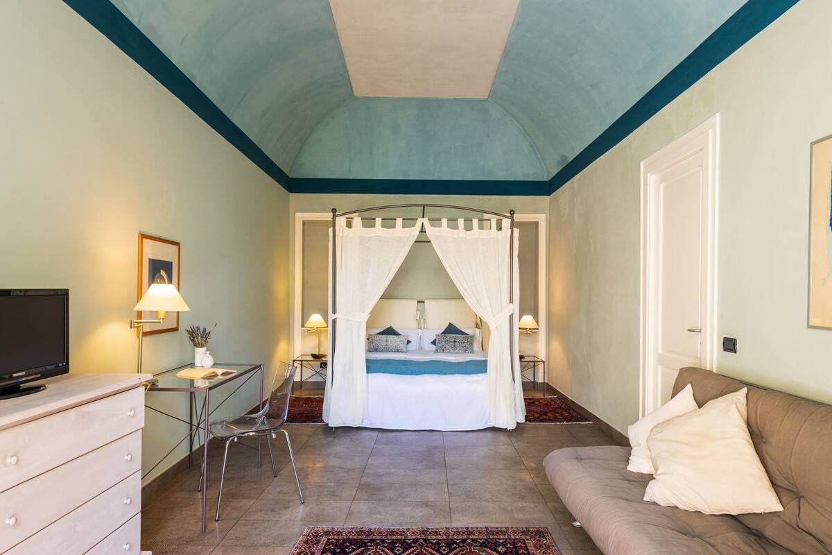 A bedroom with a bed, a TV, a desk, and a sofa.