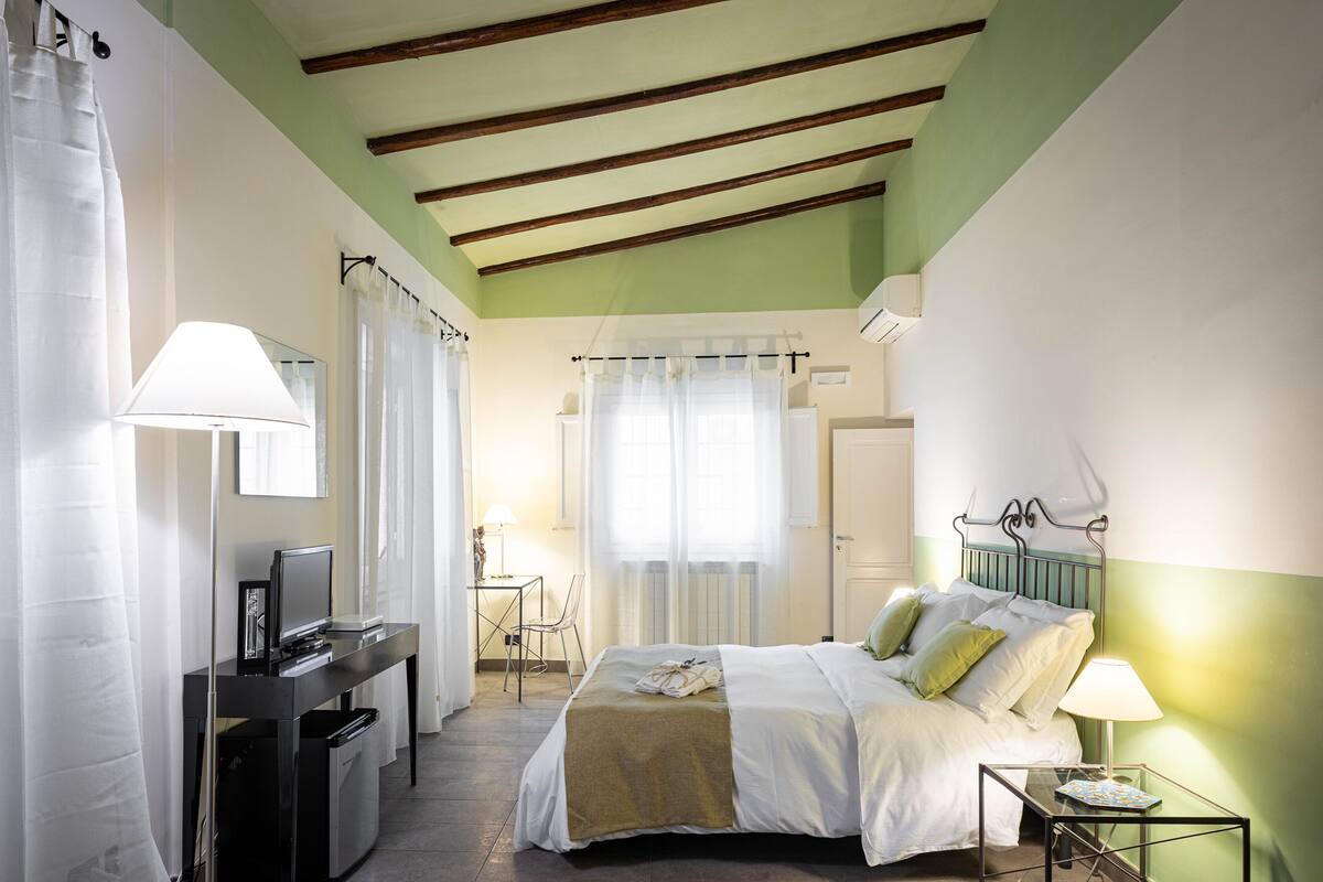 A bedroom with a bed, bedside table, lamp, and a desk with a computer.