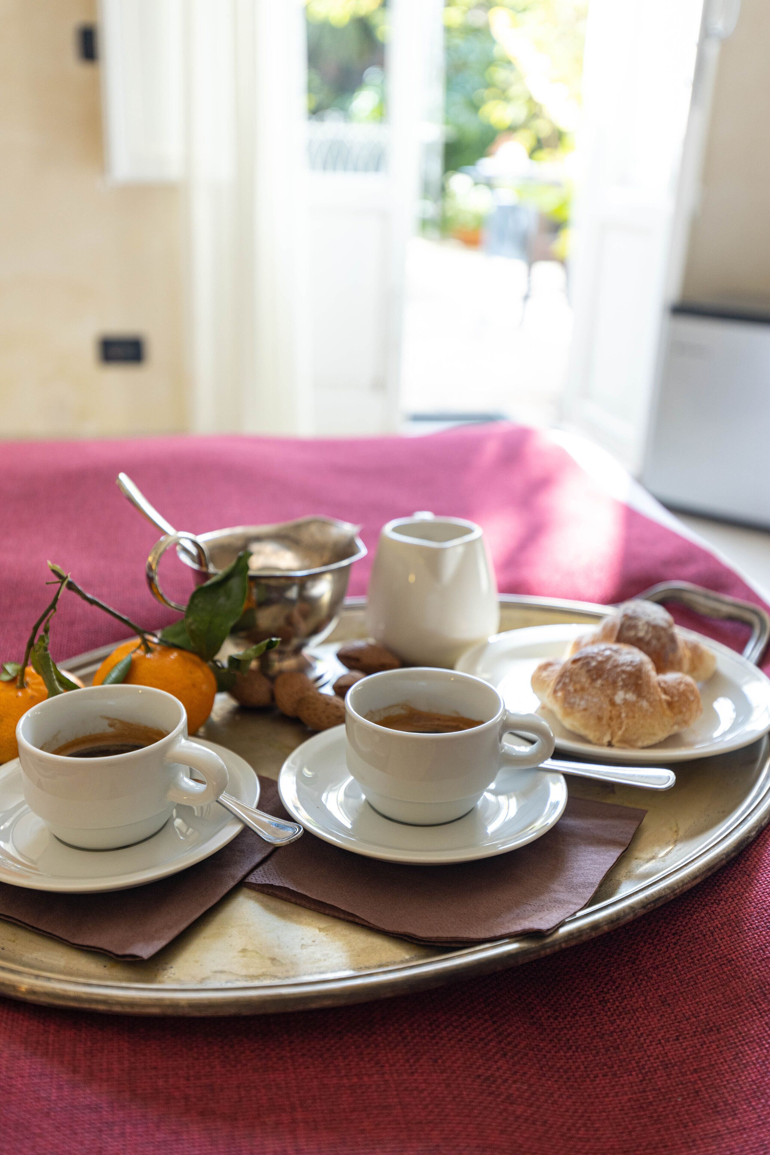 Ein Tablett mit zwei Kaffeetassen, einem Teller mit Gebäck und einer Schüssel mit Nüssen auf einem Tisch mit rotem Tuch.