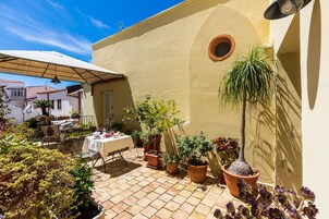 Una terrazza con tavolo apparecchiato per mangiare, circondata da piante in vaso e un ombrellone.