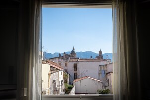 Una vista attraverso una finestra con tende, che mostra una skyline con edifici e montagne sullo sfondo.