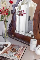 Una stanza con una toeletta in legno, uno specchio, un vaso con fiori, un libro e una tazza.