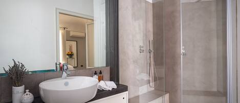 Een moderne badkamer met een grote witte wastafel, een glazen douchecabine en een spiegel met een zwarte lijst.