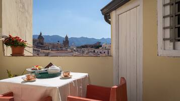 Un balcón con una mesa dispuesta para el té, con vistas a un paisaje urbano y montañas al fondo.