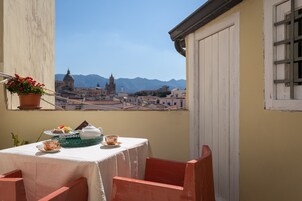Un balcon avec une table dressée pour le thé, d’où l’on peut admirer un paysage urbain avec des montagnes en arrière-plan.