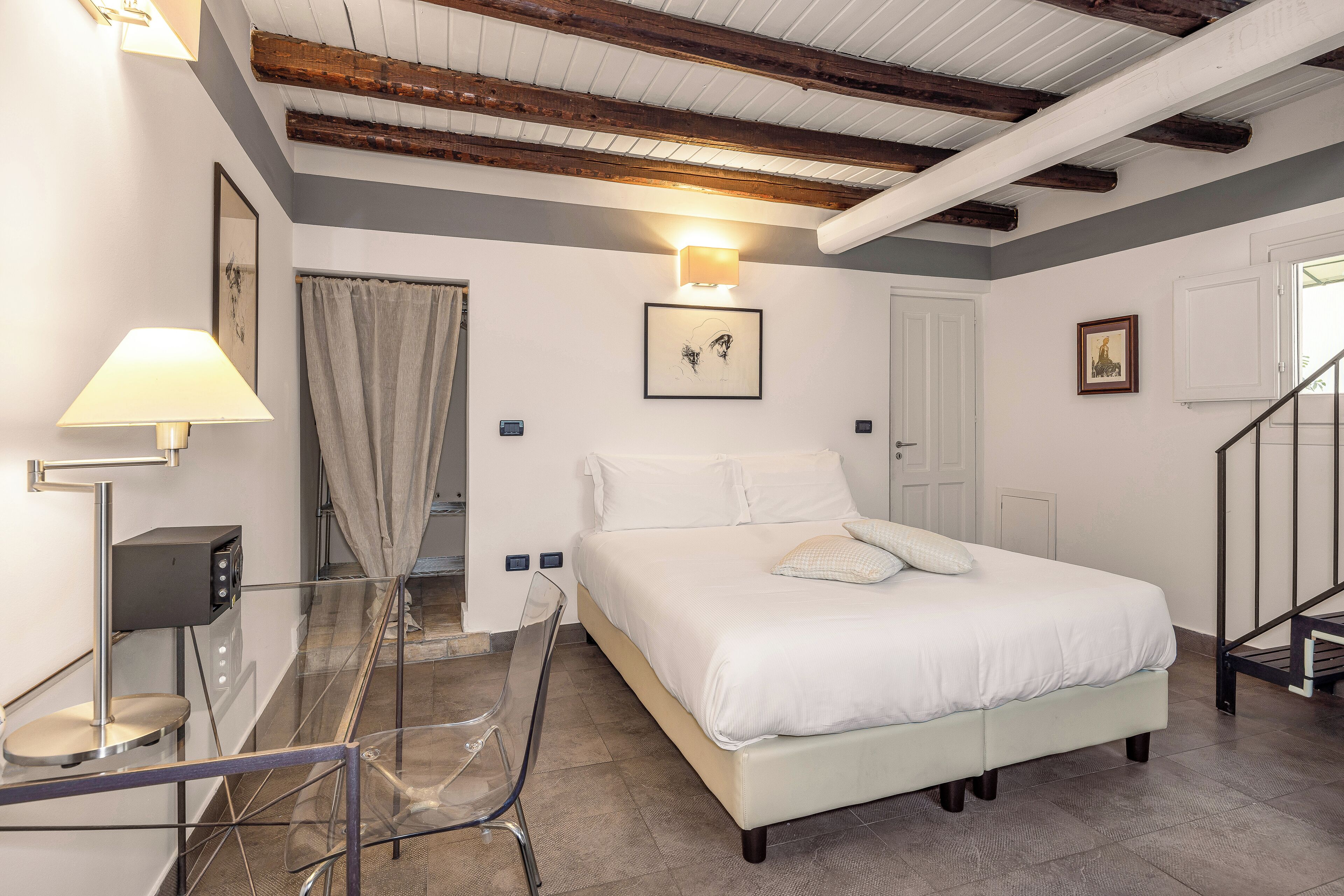 A bedroom with a bed, a desk with a lamp, a chair, a staircase, and a door.